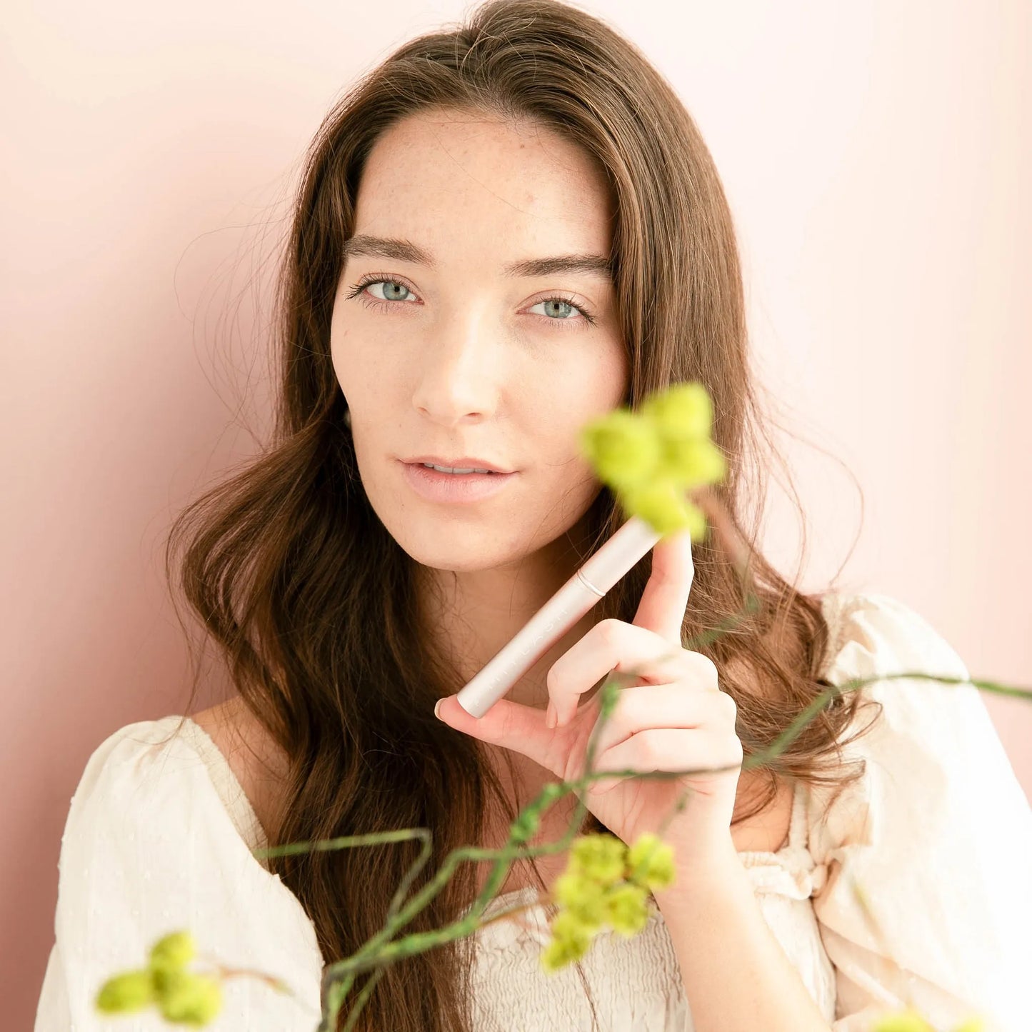 MiyLash Travel Eyelash Volumizing Growth Serum in soft pink setting with flowers, highlighting the natural, vegan formula for lash and brow enhancement.